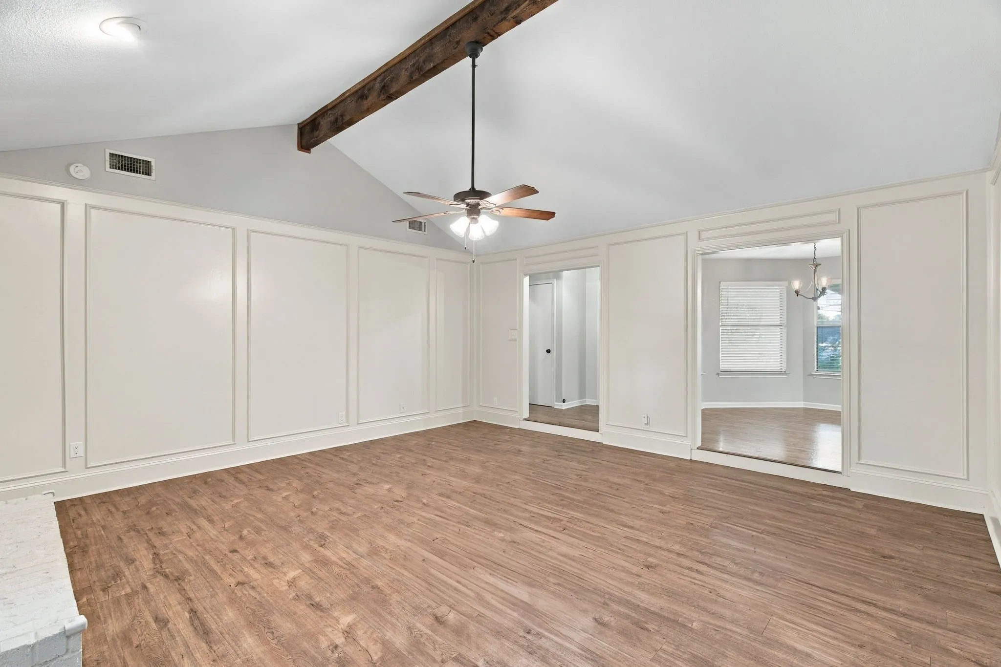 Vaulted ceiling with exposed wood beam, wood-finish flooring, architectural wall paneling, and an overhead ceiling fan