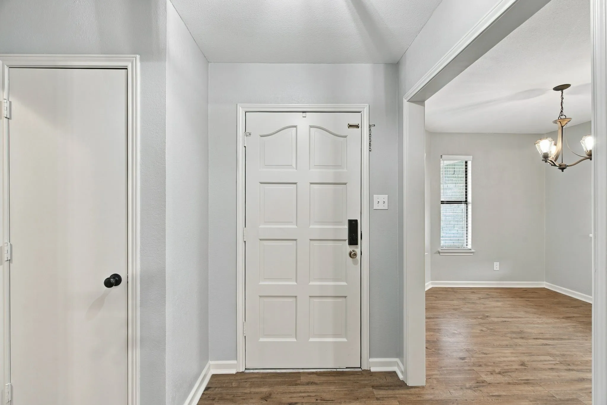 Wood-finish flooring throughout, white paneled doors, and a decorative chandelier