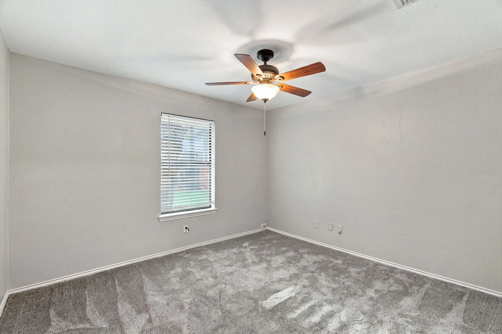 Window with white blinds, wood-finish ceiling fan with integrated lighting, light gray walls, and gray carpet
