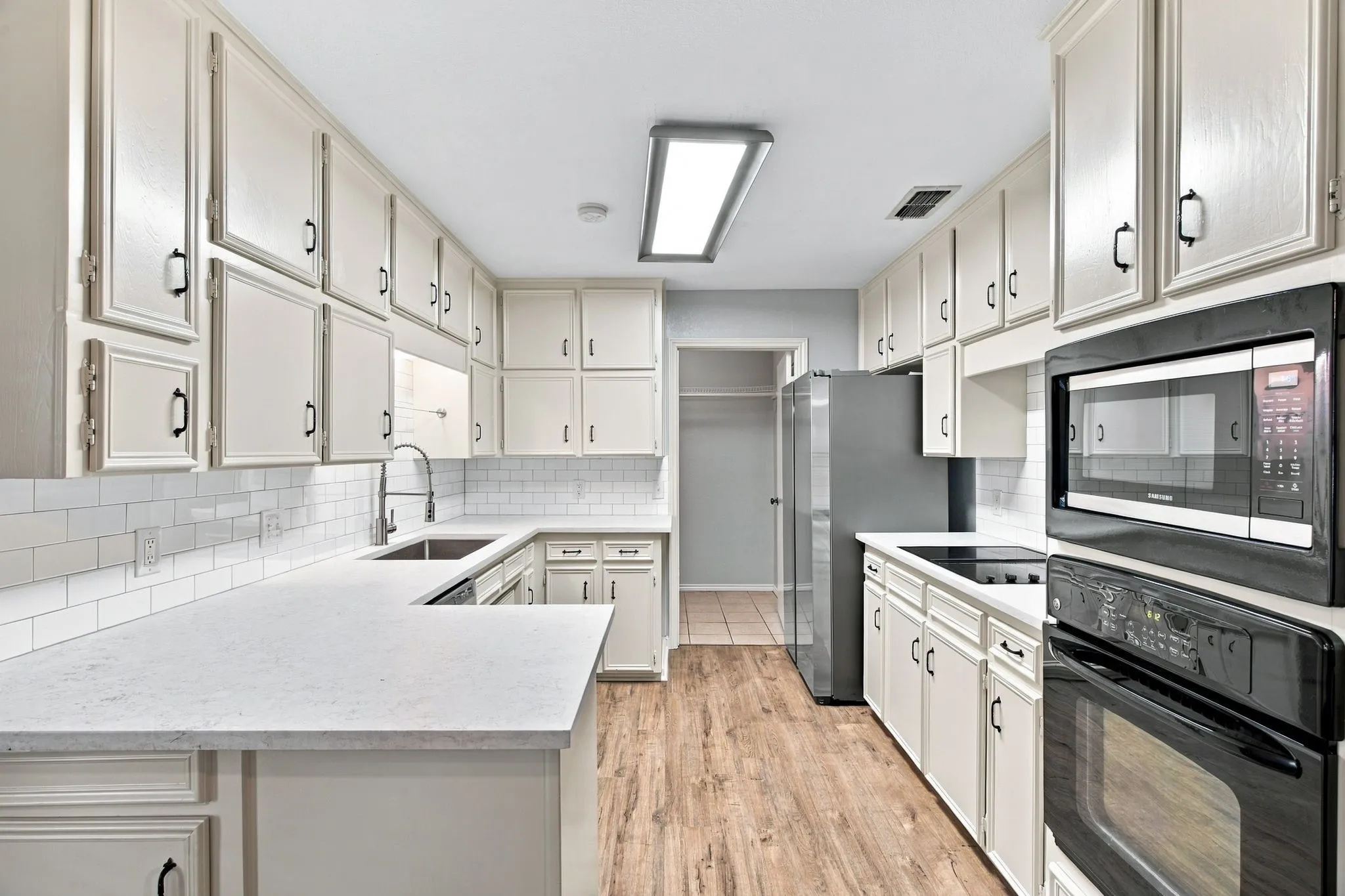 White cabinetry, white subway tile backsplash, light-toned countertops, black appliances, and wood-finish flooring