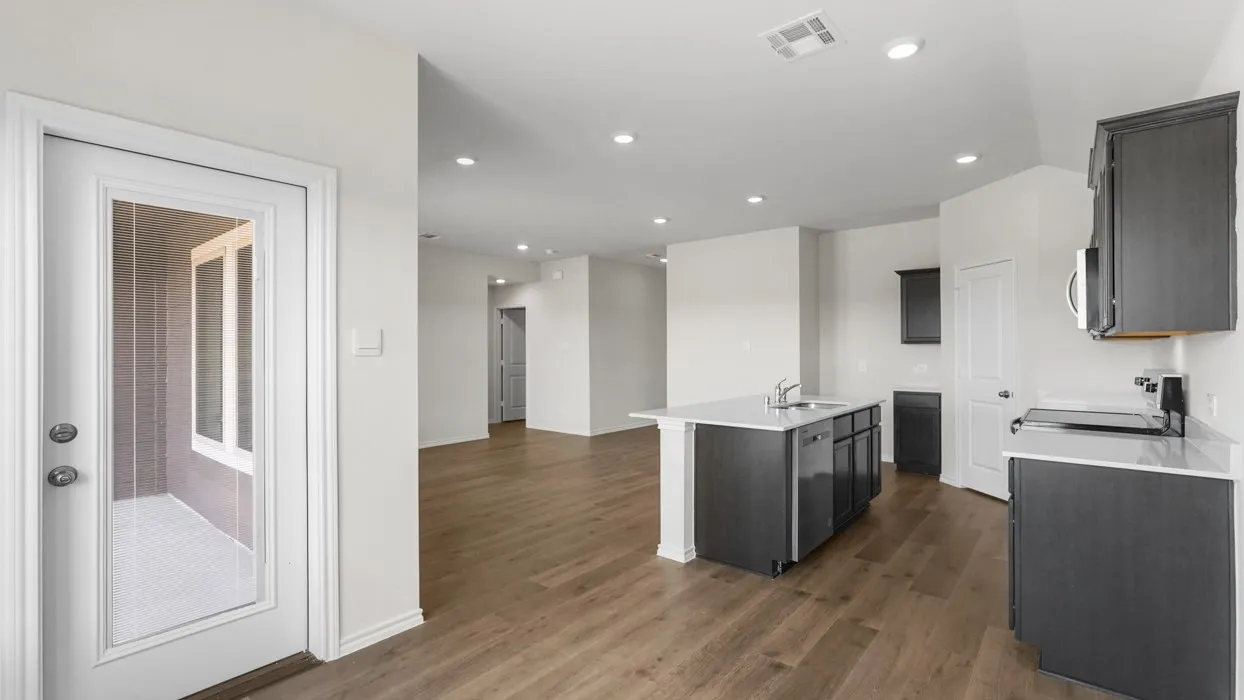 Open-concept kitchen with dark wood-finish cabinetry, a central island featuring a stainless steel sink, and light-colored countertops