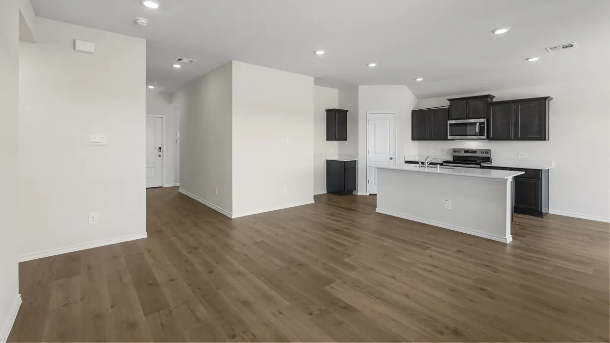 Spacious interior featuring wood-finish flooring, recessed lighting, a kitchen island with a sink, stainless steel appliances, and dark-stained cabinetry