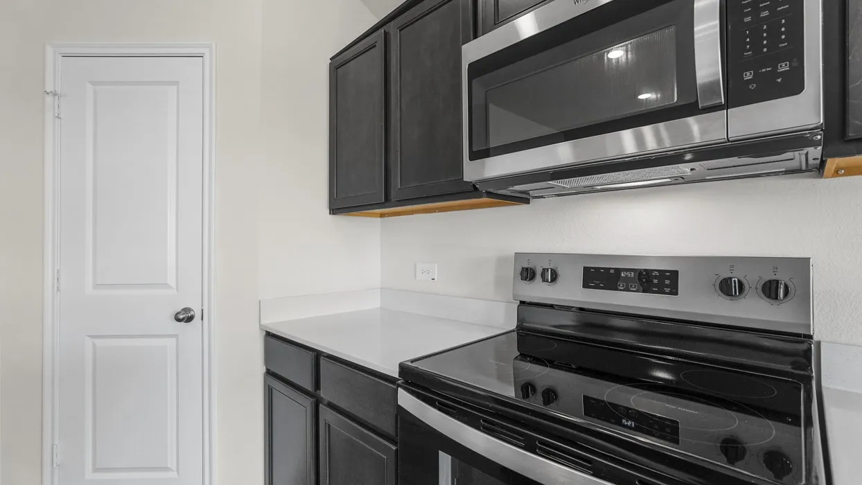 Stainless steel microwave, electric range, dark wood-finish cabinetry, and solid surface countertops