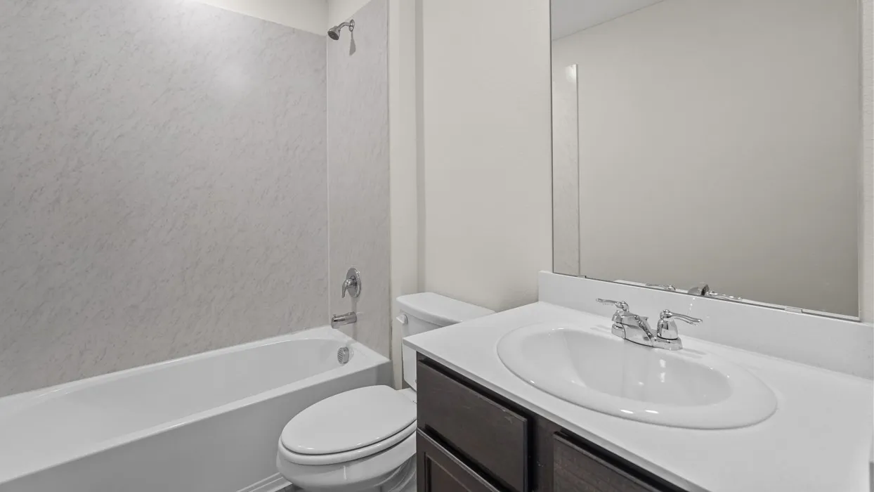 Built-in bathtub with a shower fixture, wall-mounted vanity mirror, and an undermount sink with a chrome faucet