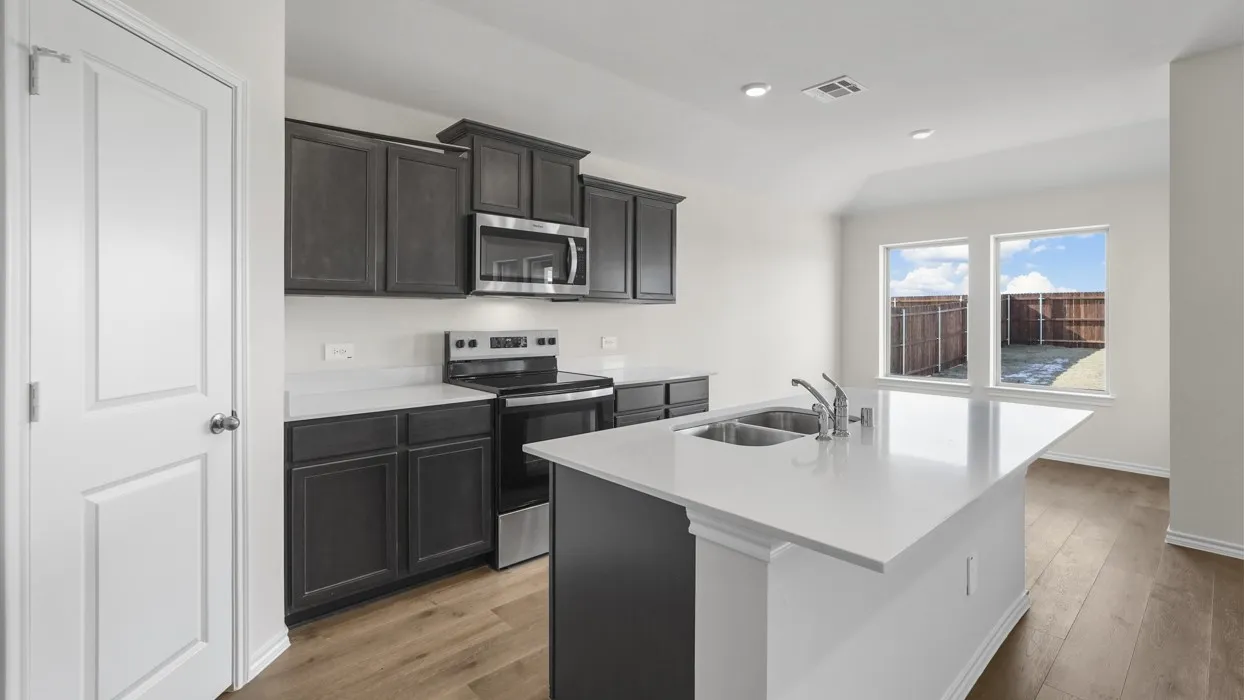 Kitchen featuring dark wood-finish cabinetry, stainless steel appliances, a white island with an integrated double sink, wood-finish flooring, and recessed lighting