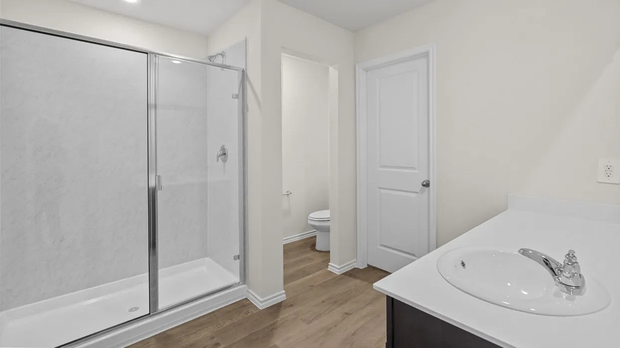 Glass-enclosed shower with a textured white surround, single vanity with an integrated sink, white countertop, and wood-finish flooring