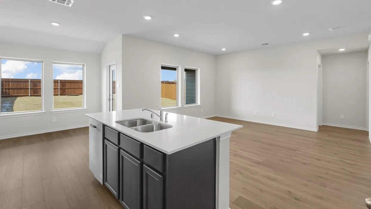 Kitchen island with dual stainless steel sink, light-toned countertops, wood-finish flooring, recessed lighting, and multiple windows