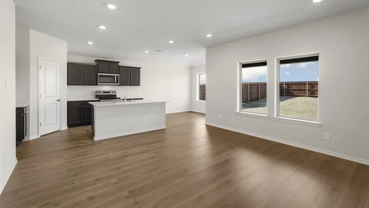 Open-concept living area with wood-finish flooring, recessed lighting, and a kitchen featuring dark cabinetry, stainless steel appliances, and a central island