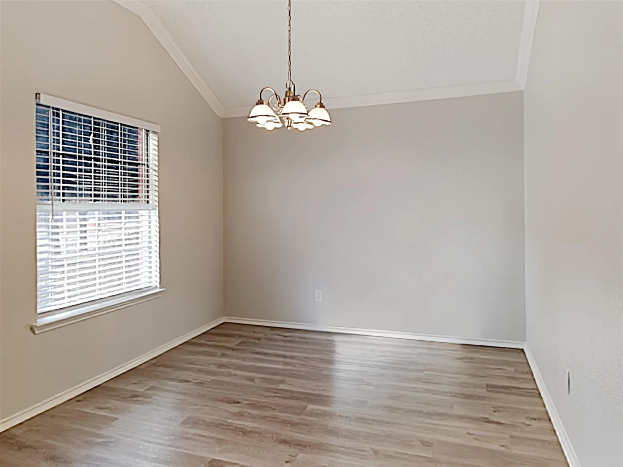 Vaulted ceiling with crown molding, wood-finish flooring, and a chandelier lighting fixture