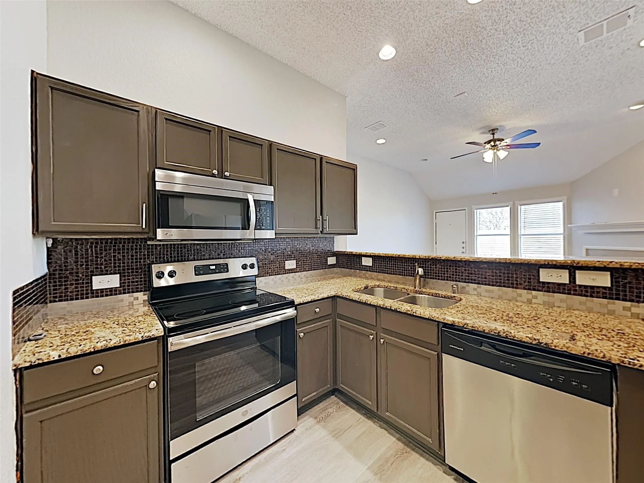 Kitchen featuring granite-style countertops, mosaic tile backsplash, stainless steel appliances, and wood-finish flooring