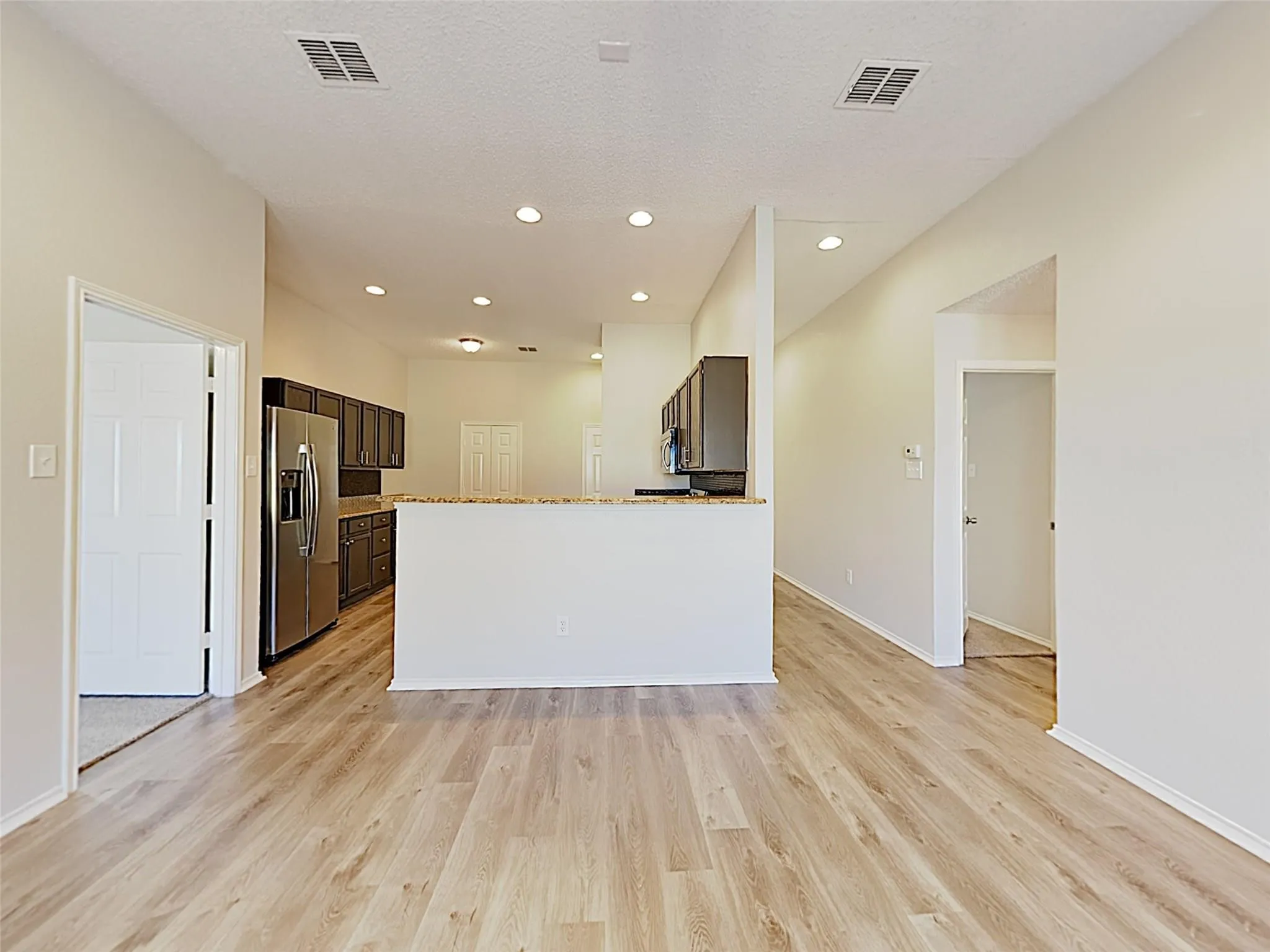 Spacious interior with wood-finish flooring, recessed lighting, and a kitchen featuring dark cabinetry, stainless steel appliances, and a pass-through counter
