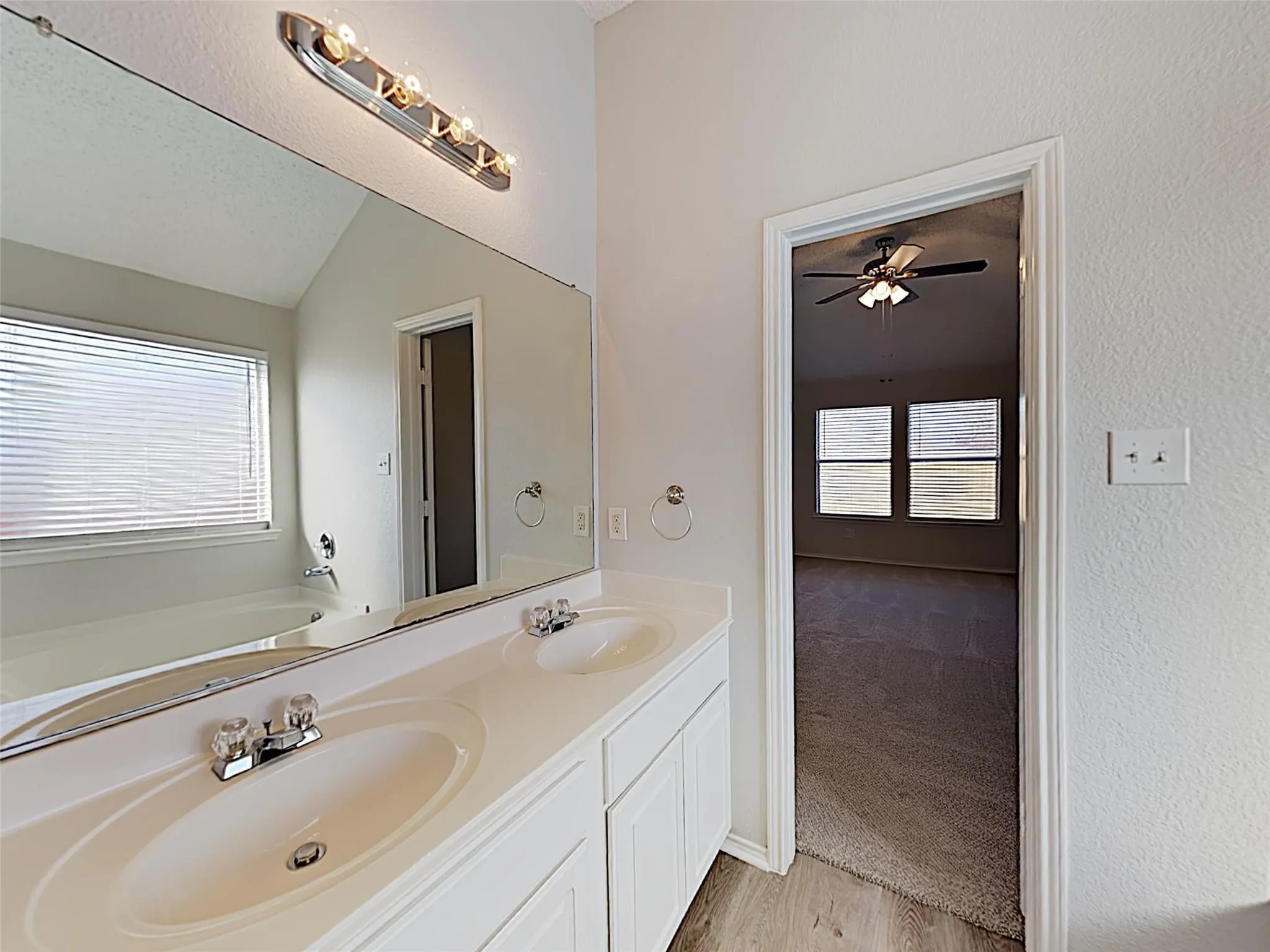 Dual vanity with white cabinetry, wood-finish flooring, and a large wall-mounted mirror