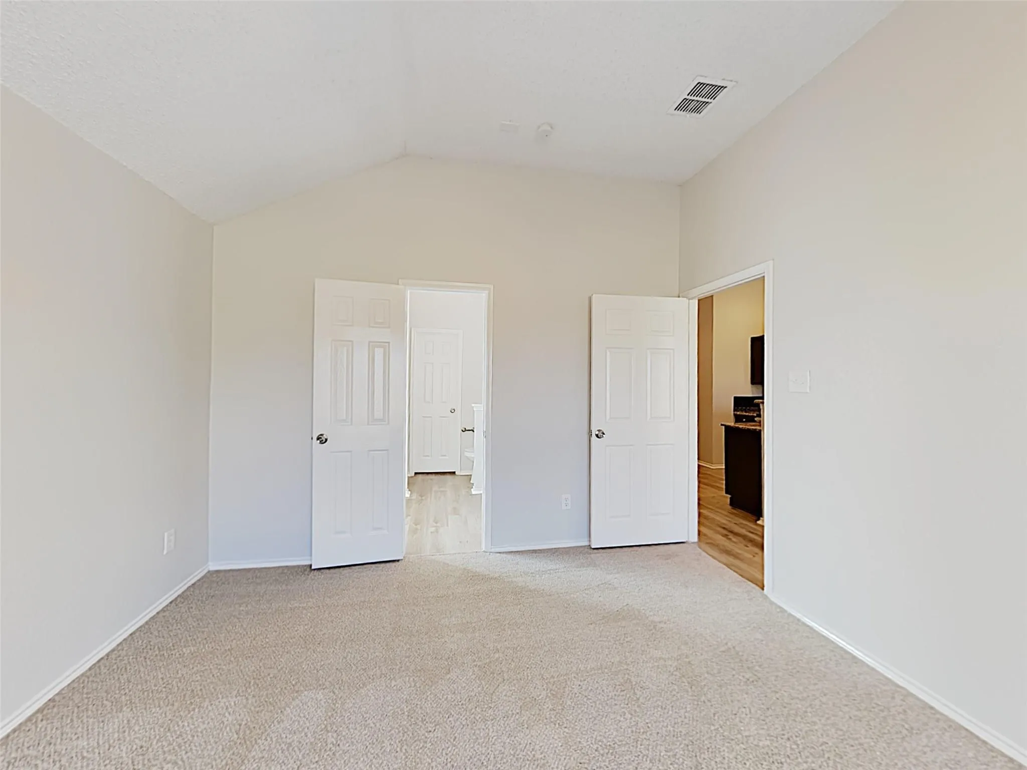 Vaulted ceiling, carpeted flooring, paneled doors, and light-toned walls