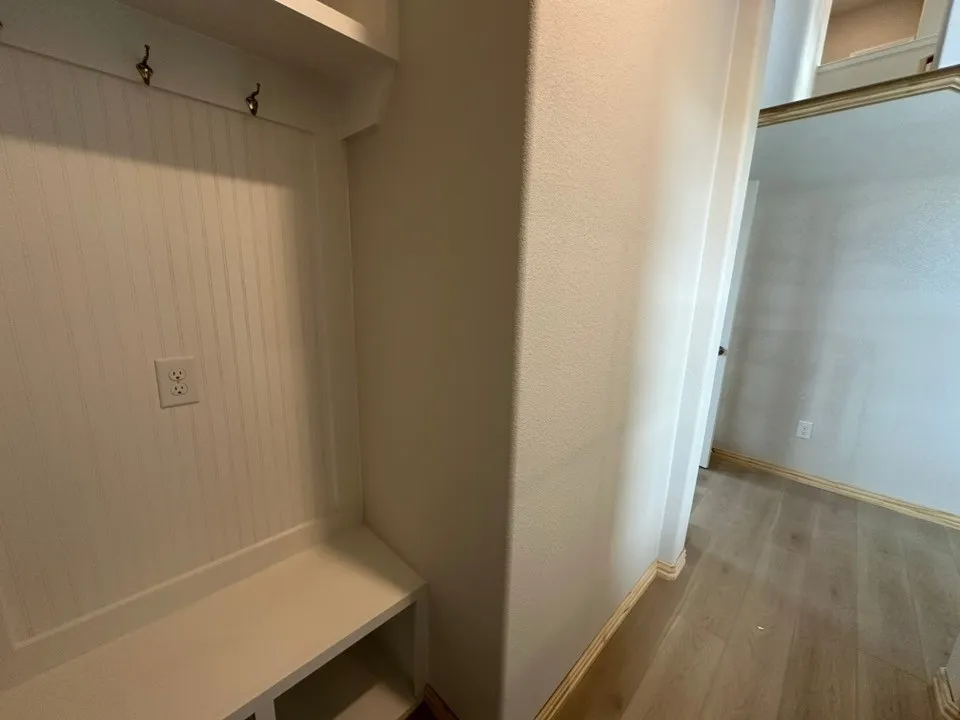 Built-in shelving with coat hooks and a bench, wood-finish flooring, and light-toned walls