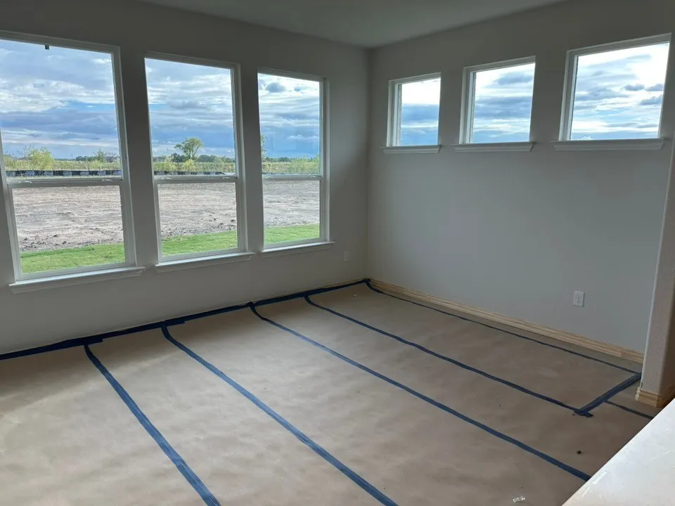 Room featuring multiple tall windows, additional upper windows, light-toned wall paint, and unfinished flooring