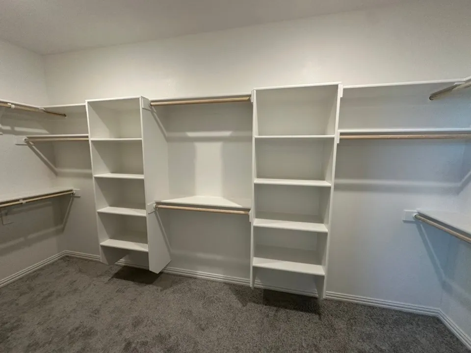 White custom built-in shelving, multiple hanging rods, and gray carpet flooring