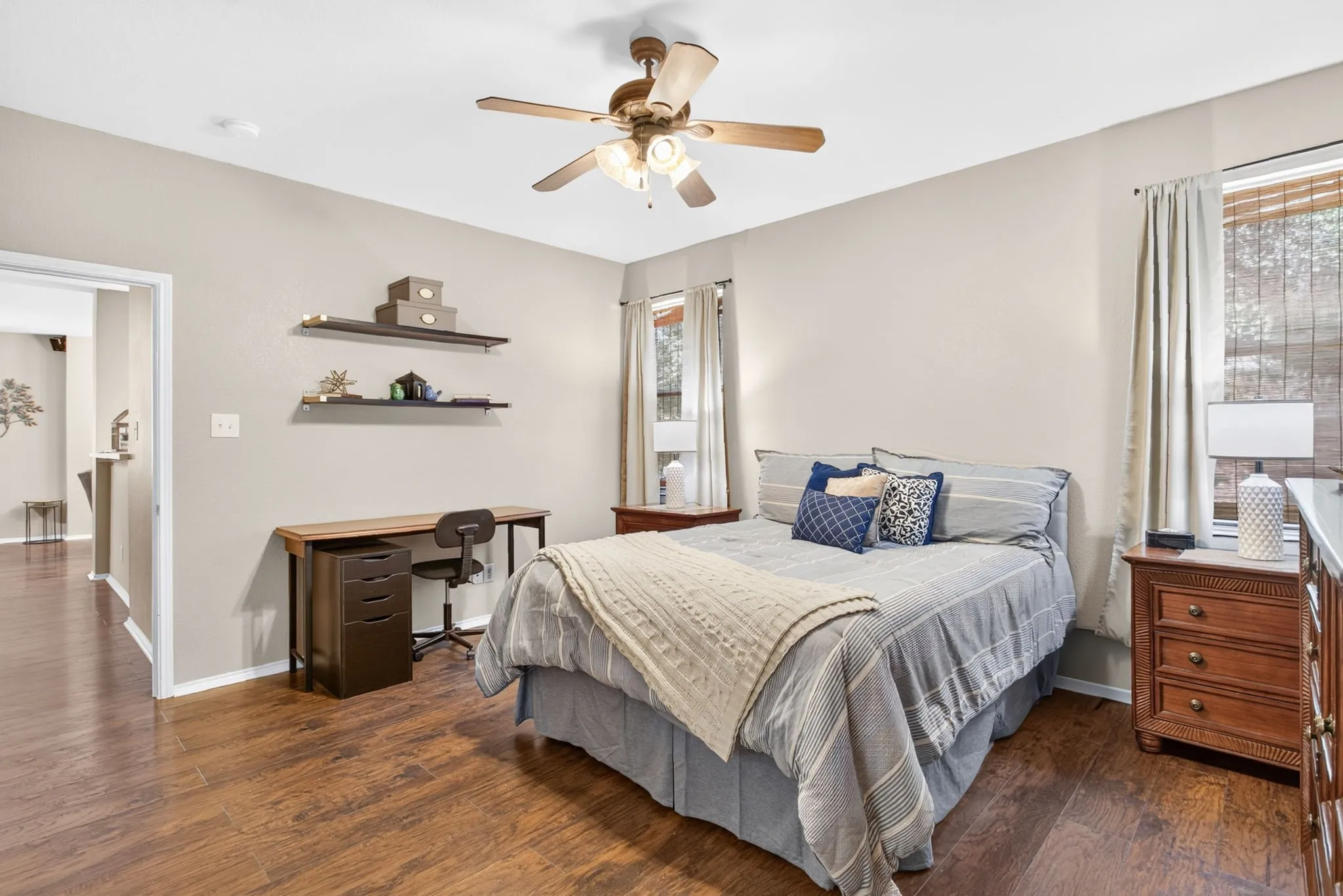 Wood-finish flooring, neutral wall tones, ceiling fan with integrated lighting, and multiple windows with blinds