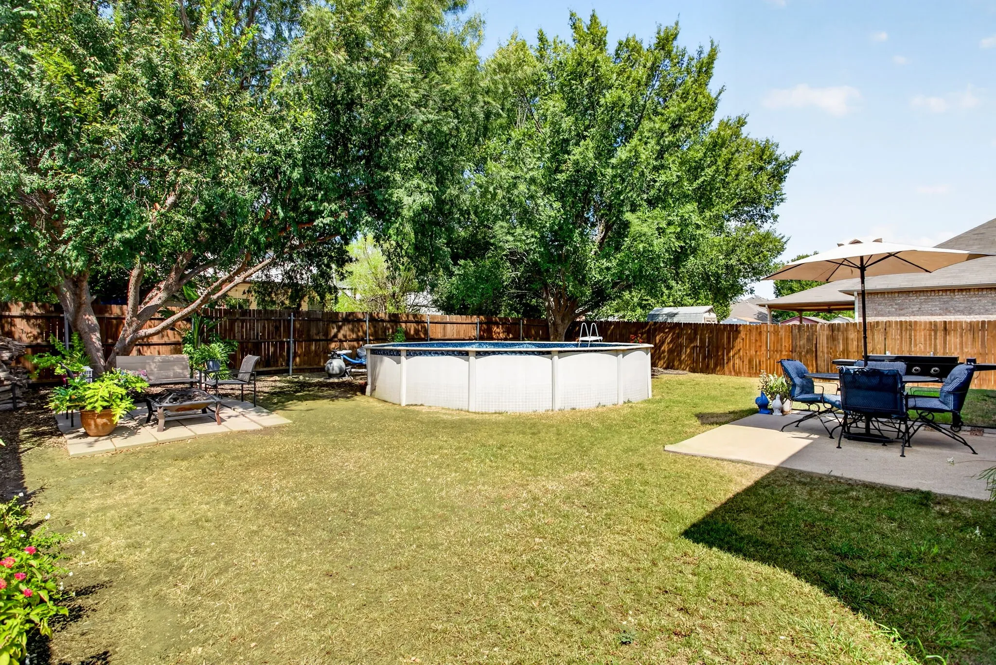 Expansive backyard featuring a manicured lawn, established trees, privacy fencing, an above-ground swimming pool, and a concrete patio