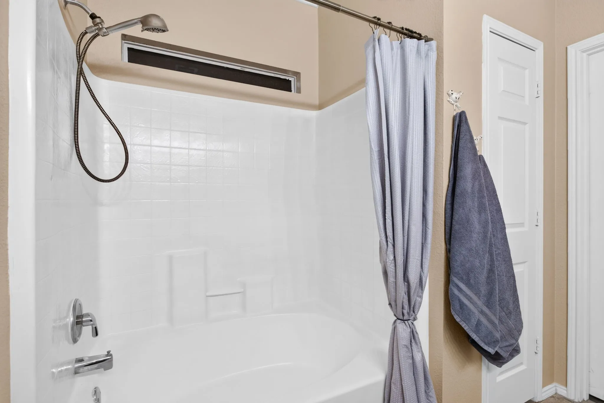 Tub and shower combination with a handheld shower head, chrome fixtures, and a white tile-patterned surround