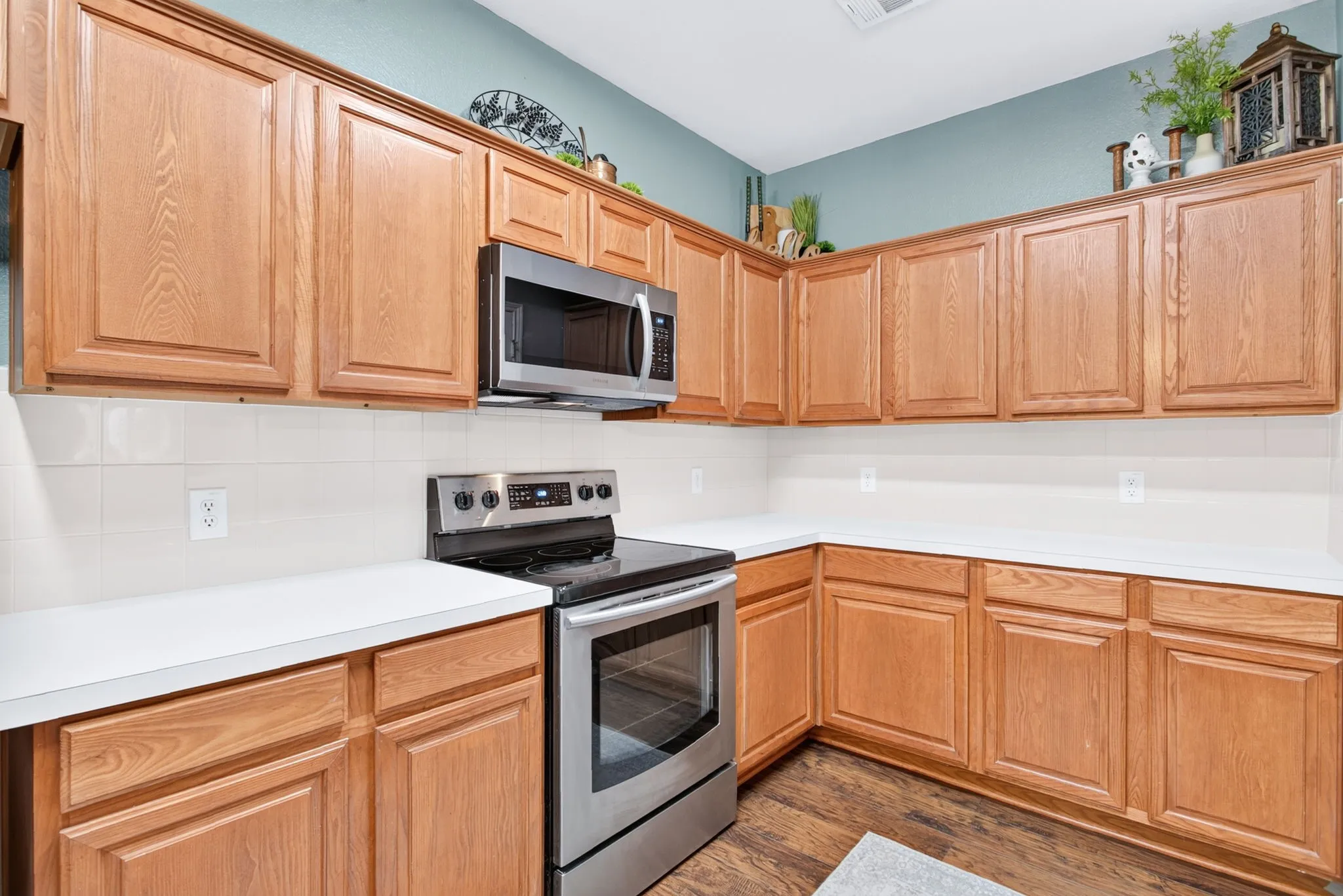 Wood-finish cabinetry, stainless steel range, stainless steel microwave, white countertops, and tile backsplash