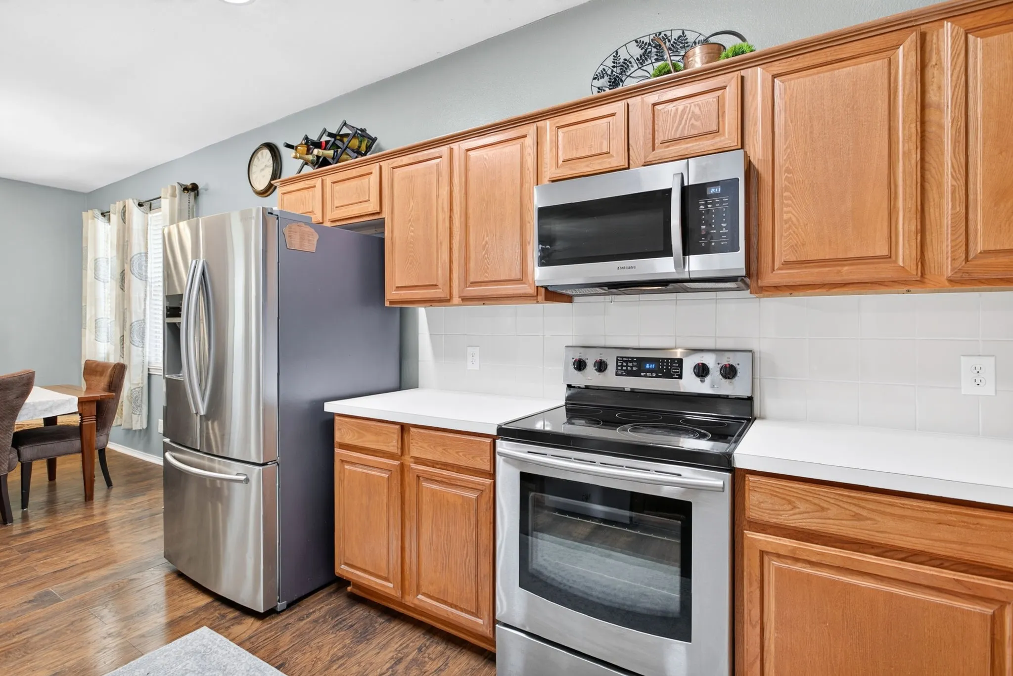 Stainless steel appliances, wood-finish flooring, white countertops, and light wood cabinetry