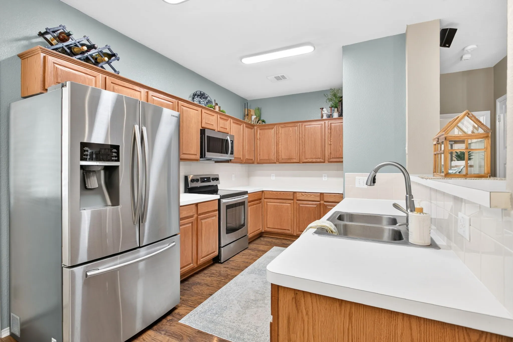 Kitchen featuring wood-finish flooring, stainless steel appliances, a double basin sink with a high-arc faucet, white countertops, and wood cabinetry