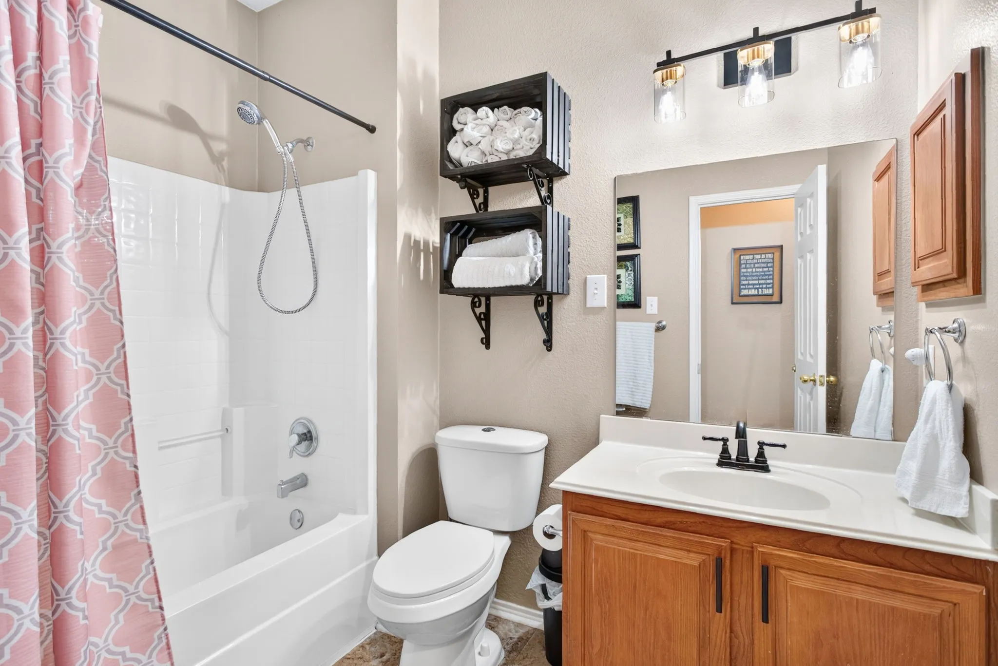 Tub/shower combination with a single-handle faucet, vanity with a rectangular undermount sink, black-finish faucet, wood-finish cabinetry, and a three-light vanity fixture