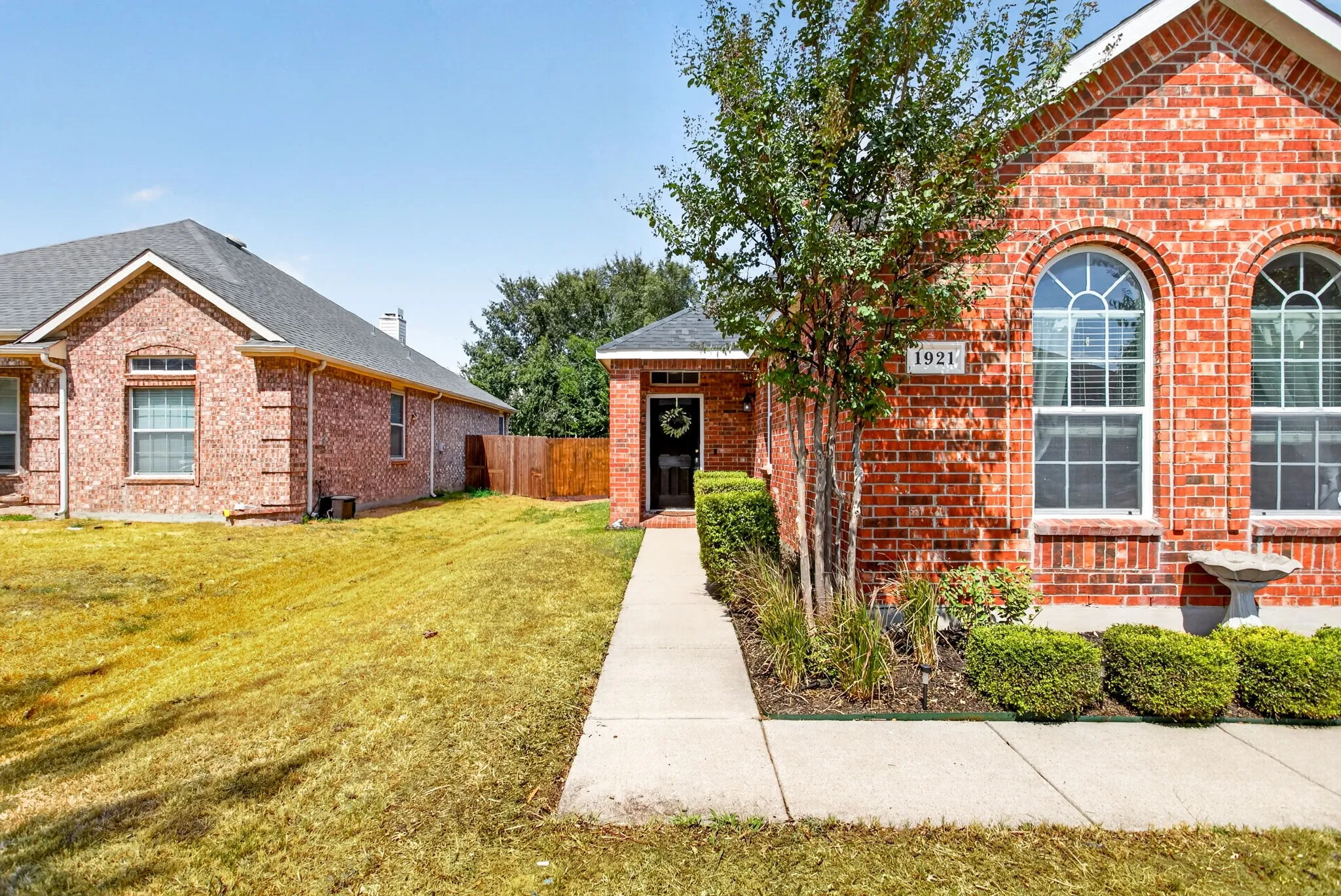 Brick exterior with arched windows, mature landscaping, and a concrete pathway