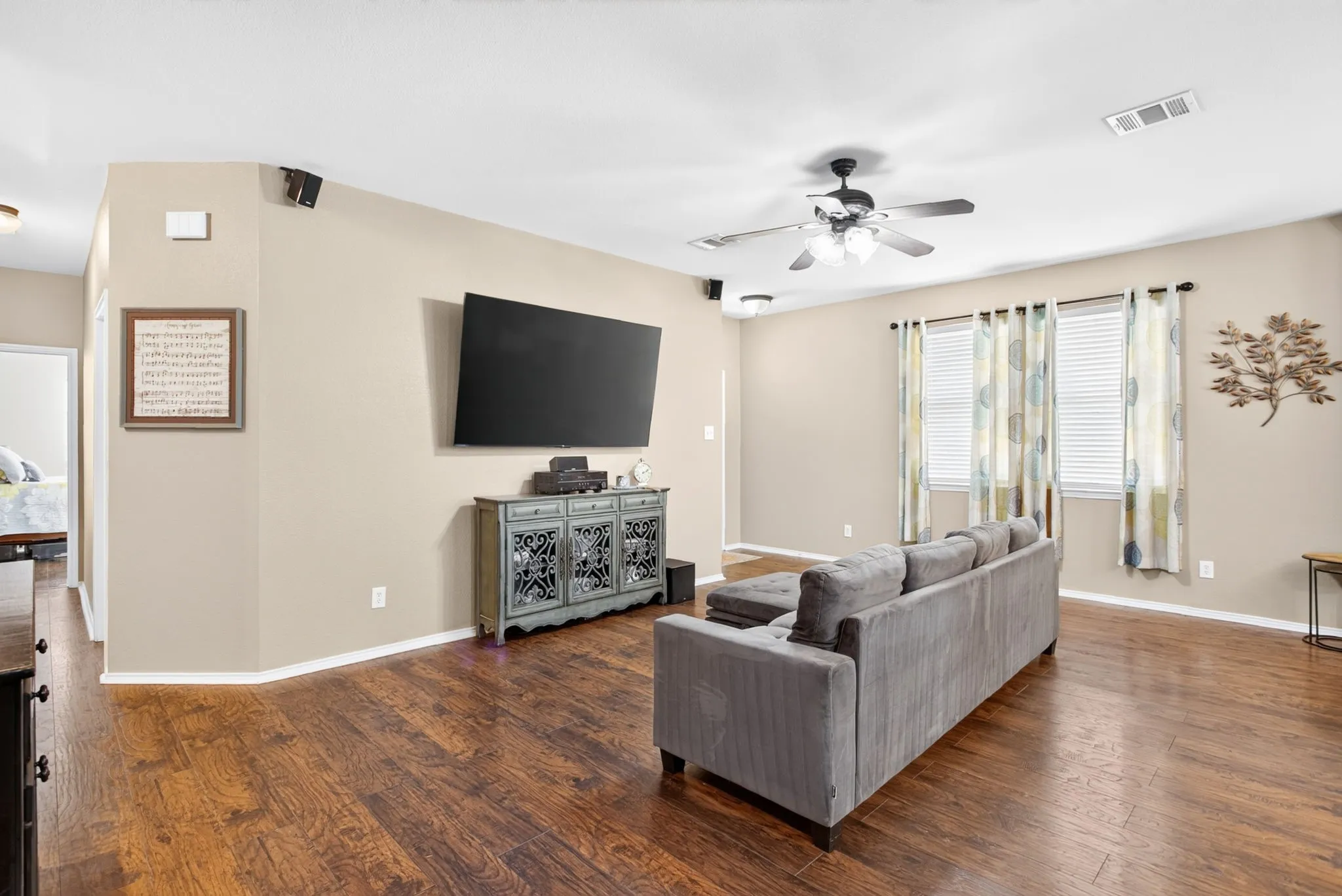 Wood-finish flooring throughout, ceiling fan with integrated lighting, and multiple windows with blinds