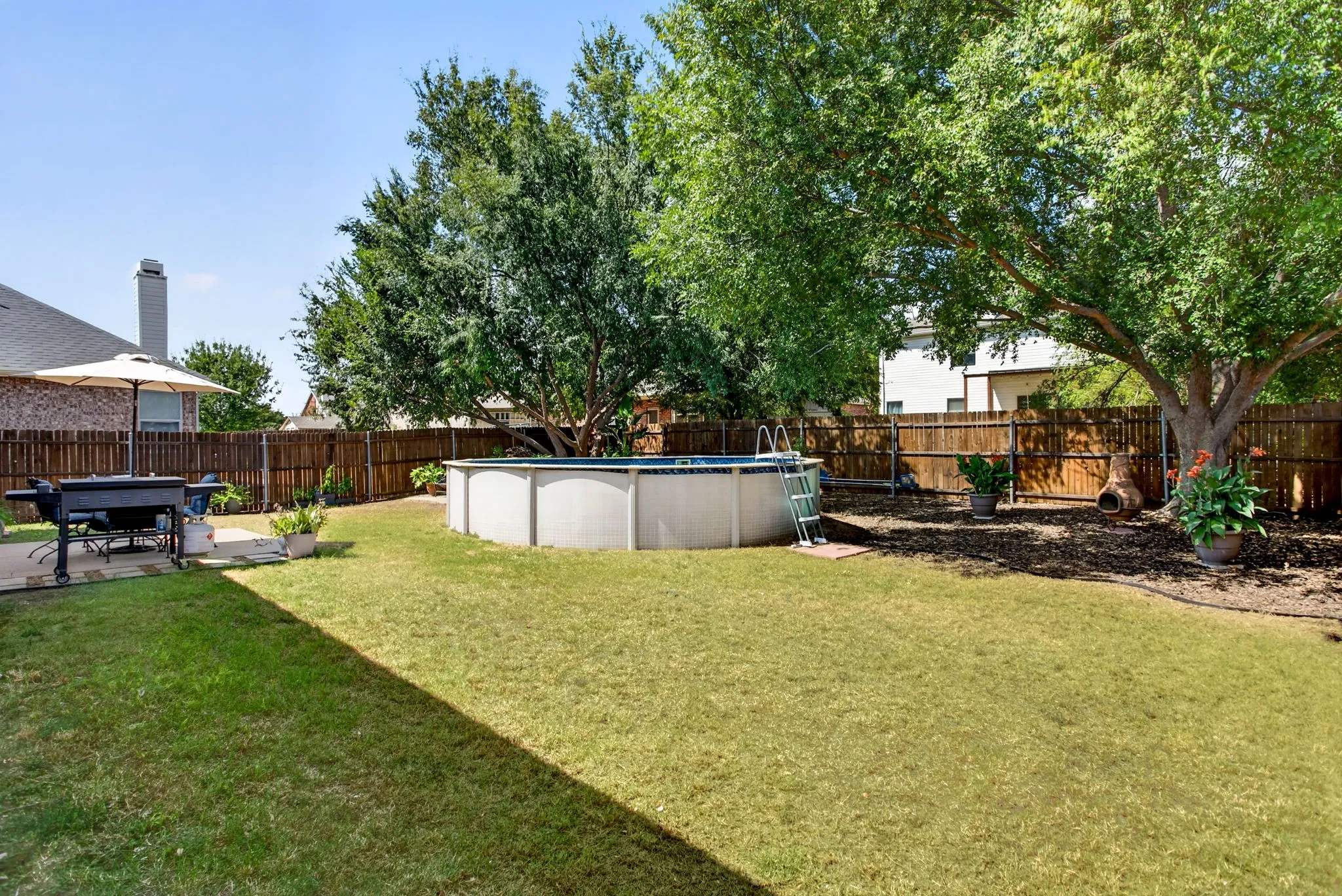 Expansive backyard featuring an above-ground pool, mature trees, and a wooden privacy fence