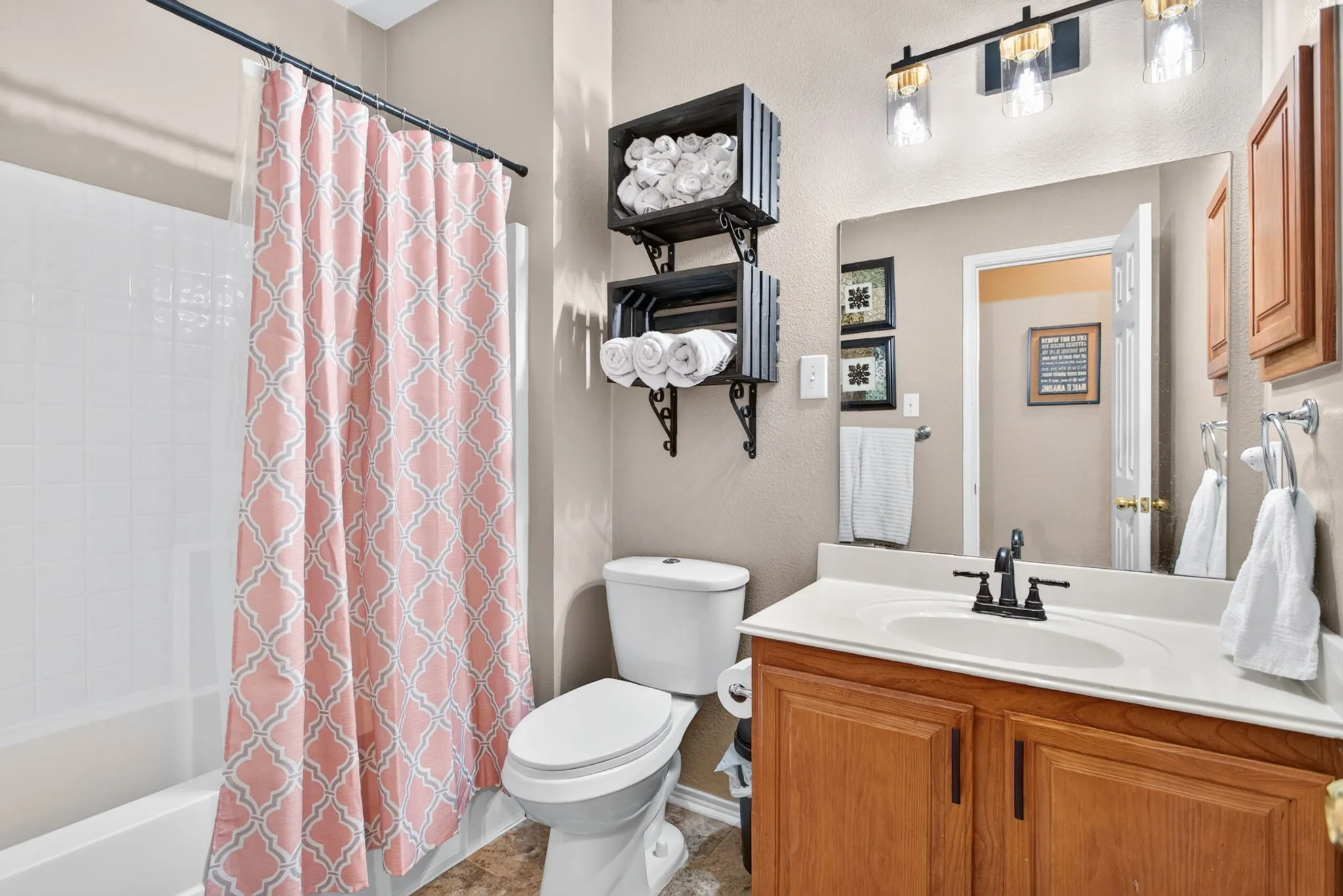 White tub with white tile surround, vanity with wood-finish cabinetry, white countertop, and integrated sink