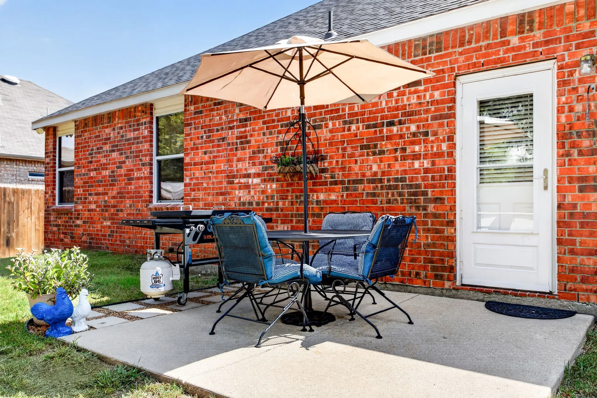 Concrete patio featuring a red brick exterior, white exterior door with glass insert, and shingled roof