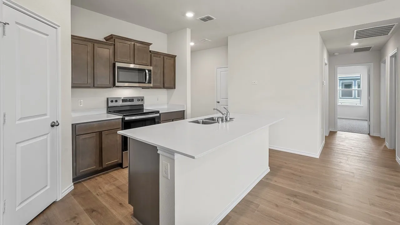 Kitchen featuring wood-finish flooring, white countertops, dark wood-finish cabinetry, stainless steel appliances, and a central island with an integrated sink