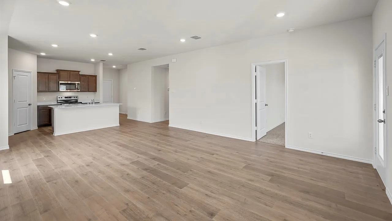 Expansive open-concept living space featuring wood-finish flooring, recessed lighting, and a kitchen with dark wood cabinetry, stainless steel appliances, and a central island with a sink
