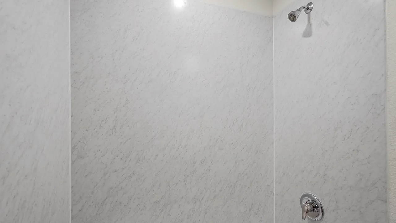 Shower enclosure featuring textured wall panels and chrome fixtures