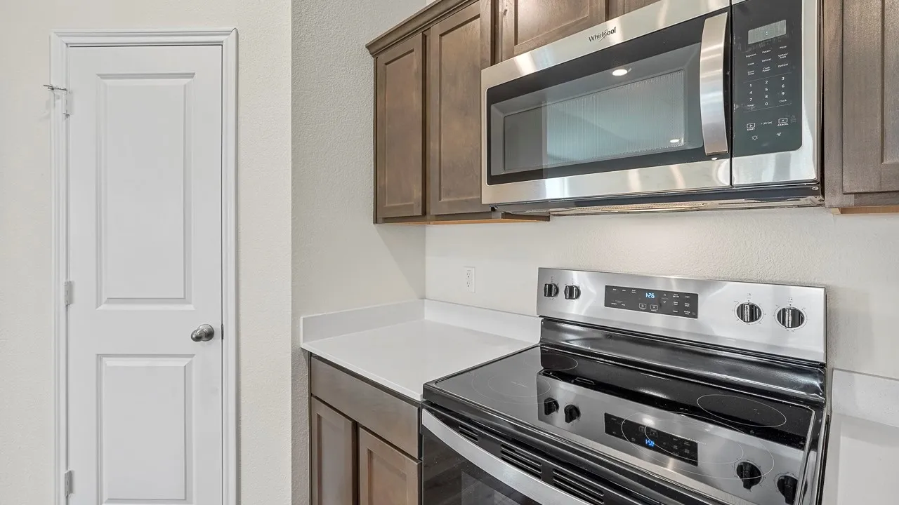 Stainless steel microwave and electric range, dark wood-finish cabinetry, and solid surface countertop