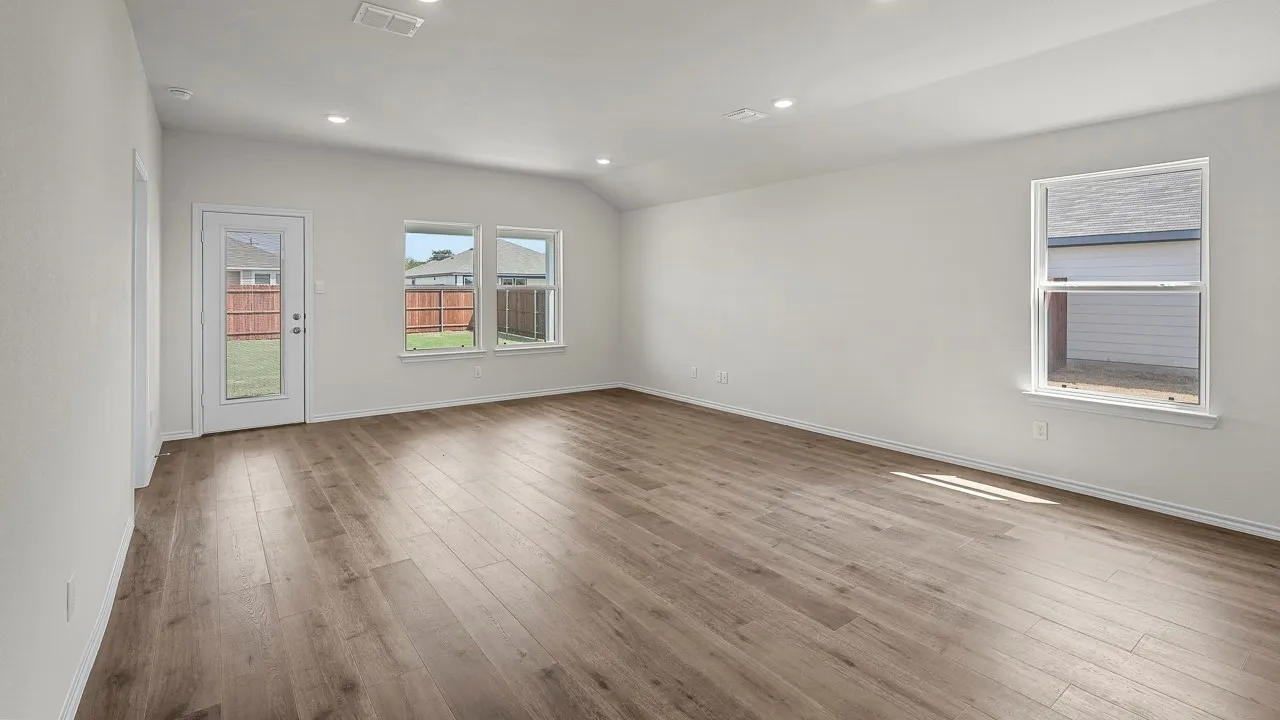Spacious room featuring wood-finish flooring, multiple windows, a glass-panel door, recessed lighting, and a vaulted ceiling