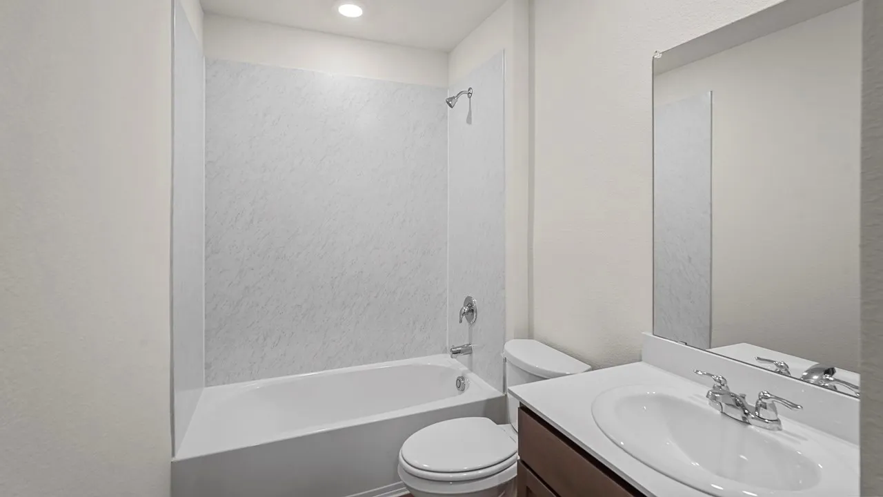 White bathtub with shower, white wall paneling, vanity with integrated sink, chrome-finish faucet, and an overhead lighting fixture