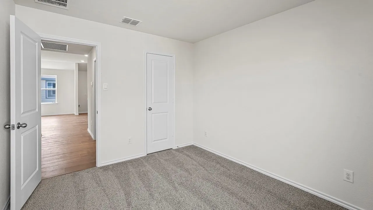 Neutral wall color, gray carpet flooring, white interior doors, and wood-finish flooring in the adjacent space