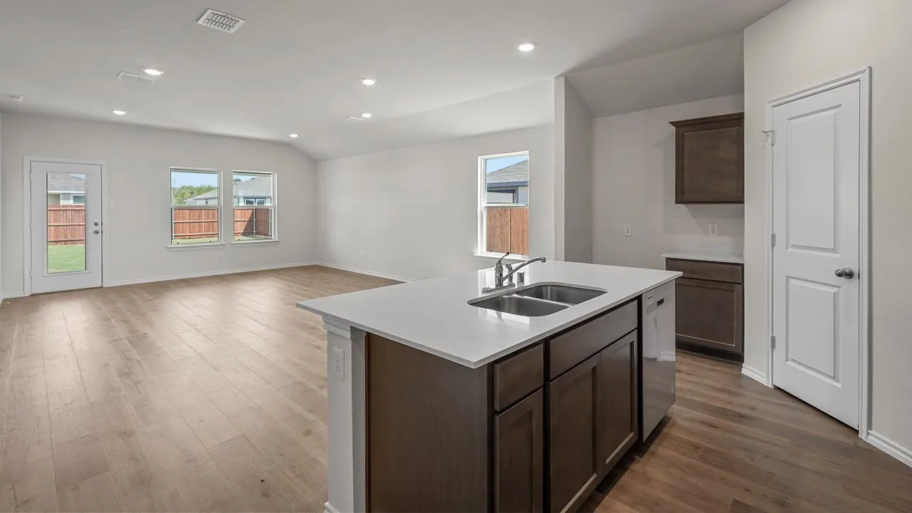 Open-concept living space with wood-finish flooring, recessed lighting, white walls, and a kitchen island featuring a double-basin sink and white countertop