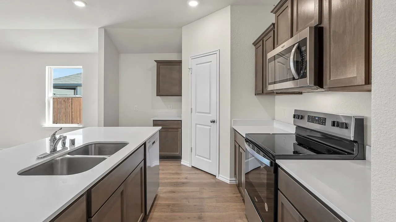 Kitchen featuring an undermount double basin sink, white countertops, wood-finish flooring, dark wood-finish cabinetry, and stainless steel appliances