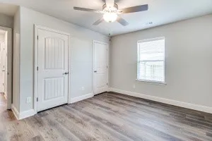 Wood-finish flooring, white paneled doors, ceiling fan with integrated lighting, and a single window with blinds