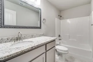 White vanity with a speckled countertop, undermount sink, and a framed mirror