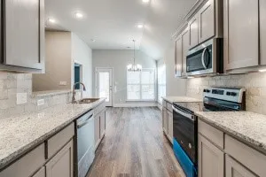 Kitchen featuring light-toned cabinetry, stainless steel appliances, speckled countertops, and a subway tile backsplash