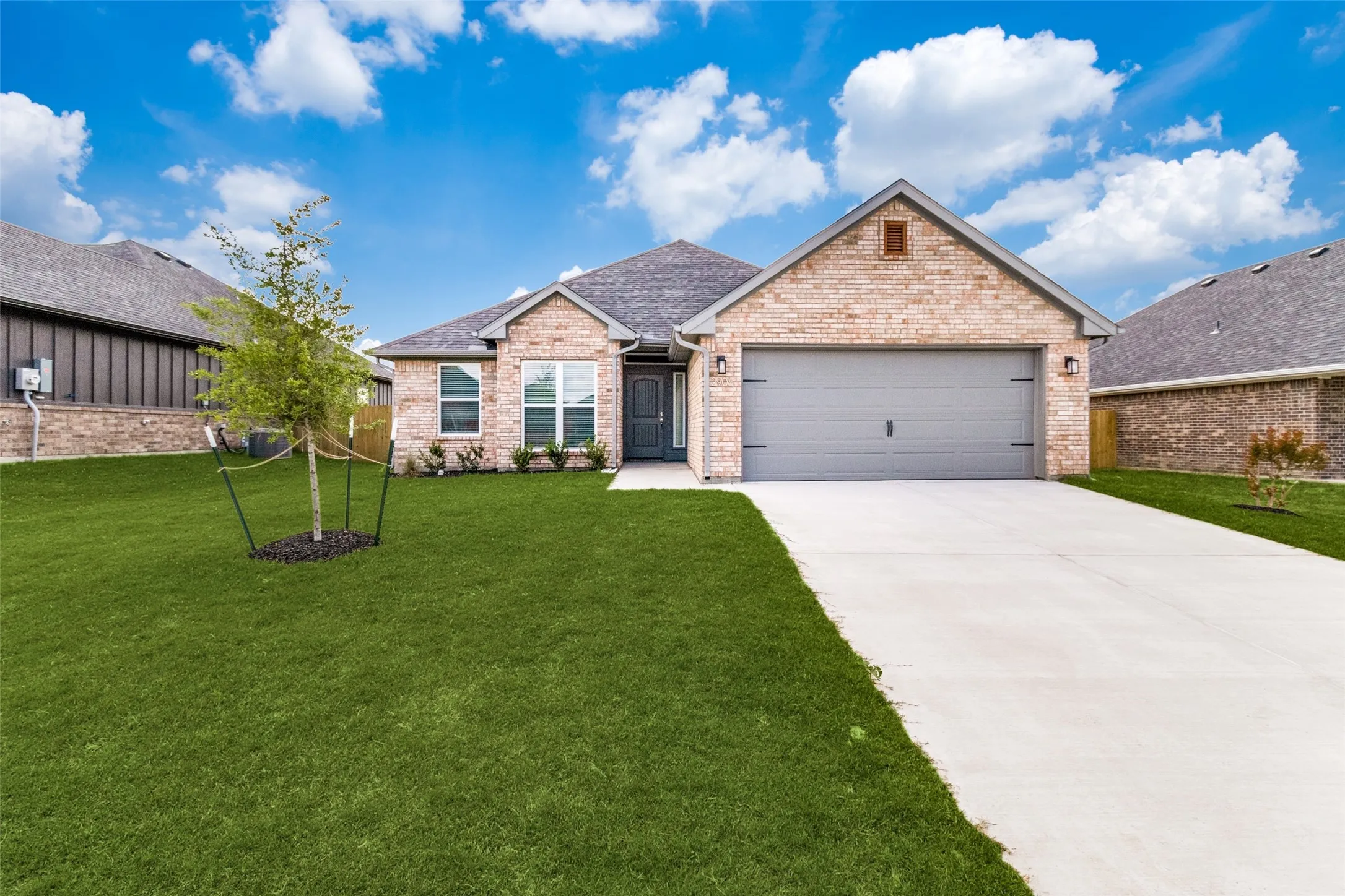 Brick exterior with a gray garage door, concrete driveway, and a manicured lawn