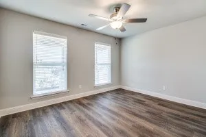 Wood-finish flooring, neutral wall tones, dual windows with blinds, and a ceiling fan with integrated lighting