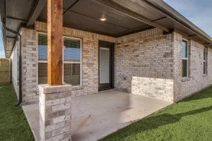 Covered patio with a concrete slab, brick exterior, and a wood support post