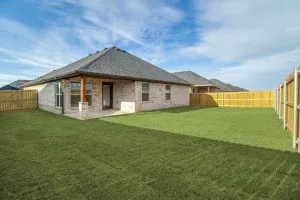 Expansive backyard featuring a manicured lawn, full privacy fencing, and a covered patio with architectural columns