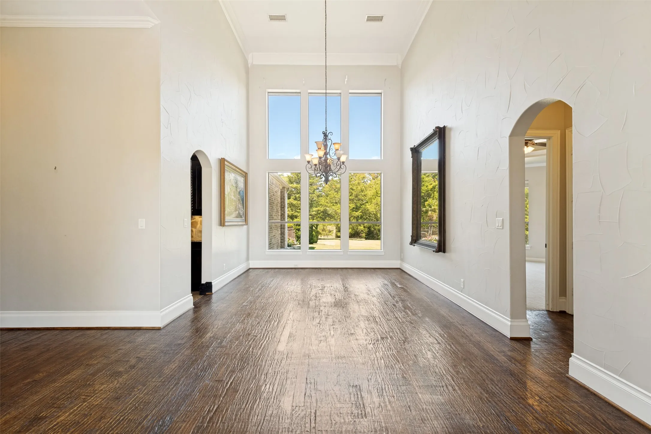 High ceilings featuring crown molding, expansive windows, wood-finish flooring, and arched doorways