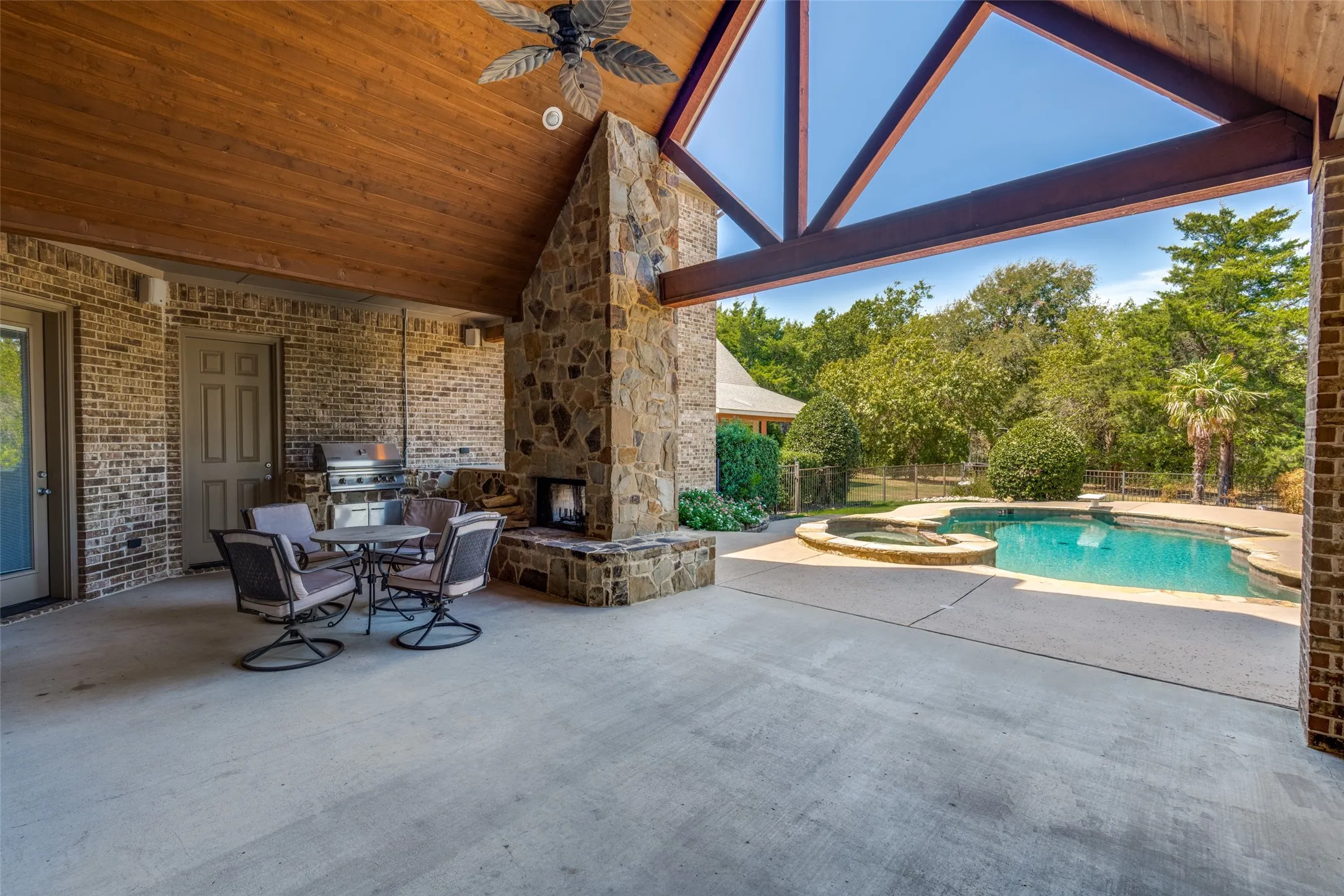 Covered patio with a wood-plank ceiling, stone fireplace, and exposed beams
